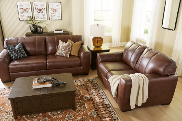 Two brown leather sofas in a living room with a patterned rug and light-colored walls.