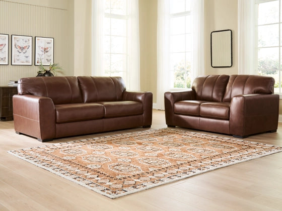 Two brown leather sofas in a living room with a patterned rug and light-colored walls.